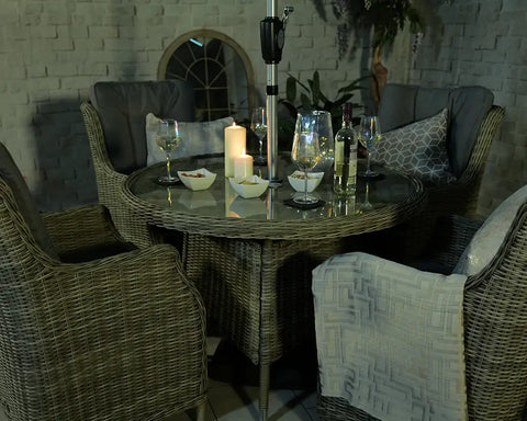 Rattan garden dining set with glass top table, cushioned chairs, wine glasses and candles