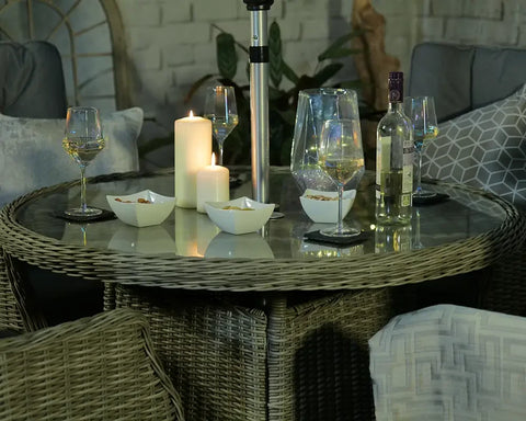 Round rattan garden dining table with glass top, wine glasses, candles and snacks