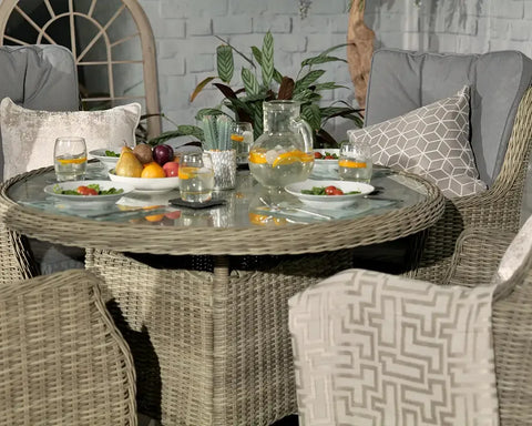 Round rattan garden dining set with glass top, grey cushions, fruit and drinks on table