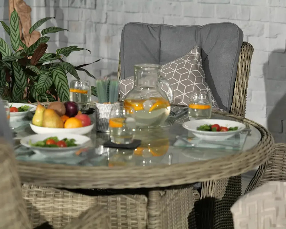 Rattan dining set with glass table, grey cushioned chair, plated fruit and salad, outdoor setting
