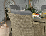 Rattan dining chair with grey cushion beside glass table set with fruit bowls and drinks