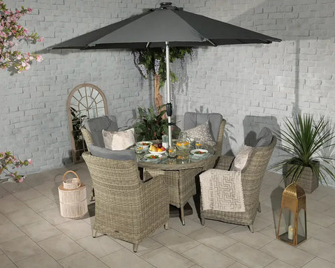 Rattan outdoor dining set with glass table, six cushioned chairs and grey parasol on patio
