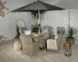 Rattan outdoor dining set with glass table, six cushioned chairs and grey parasol on patio