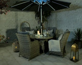 Rattan garden dining set with round table, cushioned chairs and LED parasol at night