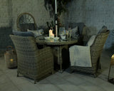 Rattan garden dining set with cushions, round glass table, candles, and wine glasses