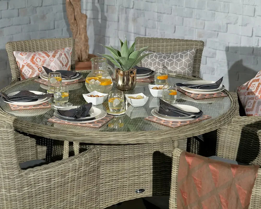 Round rattan dining table set with glass top, cushioned chairs and tableware arranged
