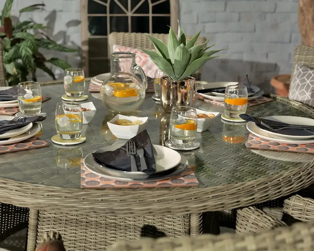Round rattan garden dining table with glass top, six place settings and drinks outdoors