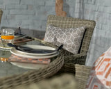 Rattan garden chair with geometric cushion beside glass-topped outdoor dining table