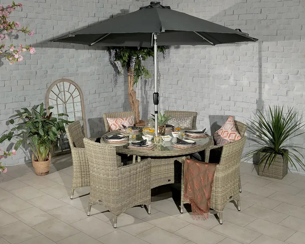 Rattan outdoor dining set with six armchairs, glass top table and large parasol on patio