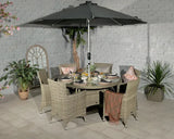 Rattan outdoor dining set with six armchairs, glass top table and large parasol on patio