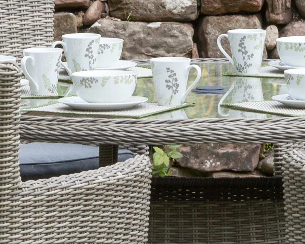 Close-up of grey rattan outdoor dining table set with glass top and tea cups