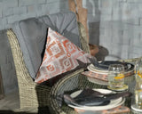 Wicker dining chair with grey cushion and patterned pillow beside glass dining table with place settings