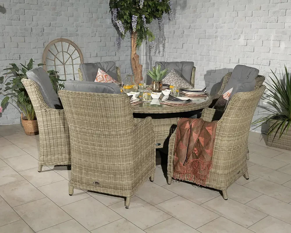 Rattan garden dining set with six cushioned chairs and round table, plants in background