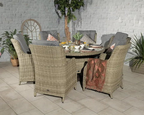 Rattan garden dining set with six cushioned chairs and round table, plants in background