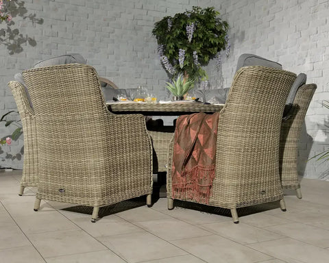 Rattan dining set with four armchairs, round table, and cushions in a garden patio setting