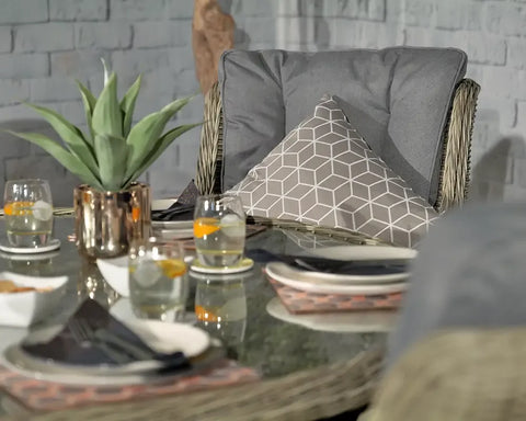Rattan garden chair with grey cushion and geometric pillow next to glass outdoor dining table