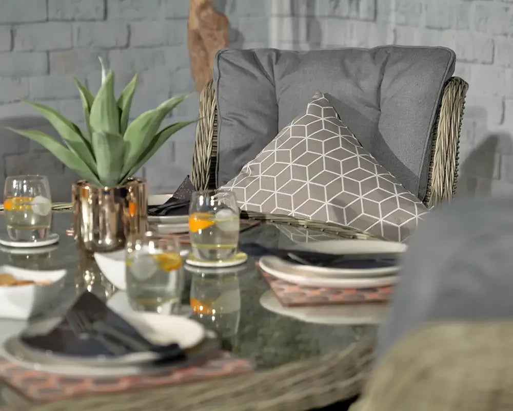 Rattan garden chair with grey cushion and geometric pillow next to glass outdoor dining table