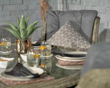 Rattan garden chair with grey cushion and geometric pillow next to glass outdoor dining table