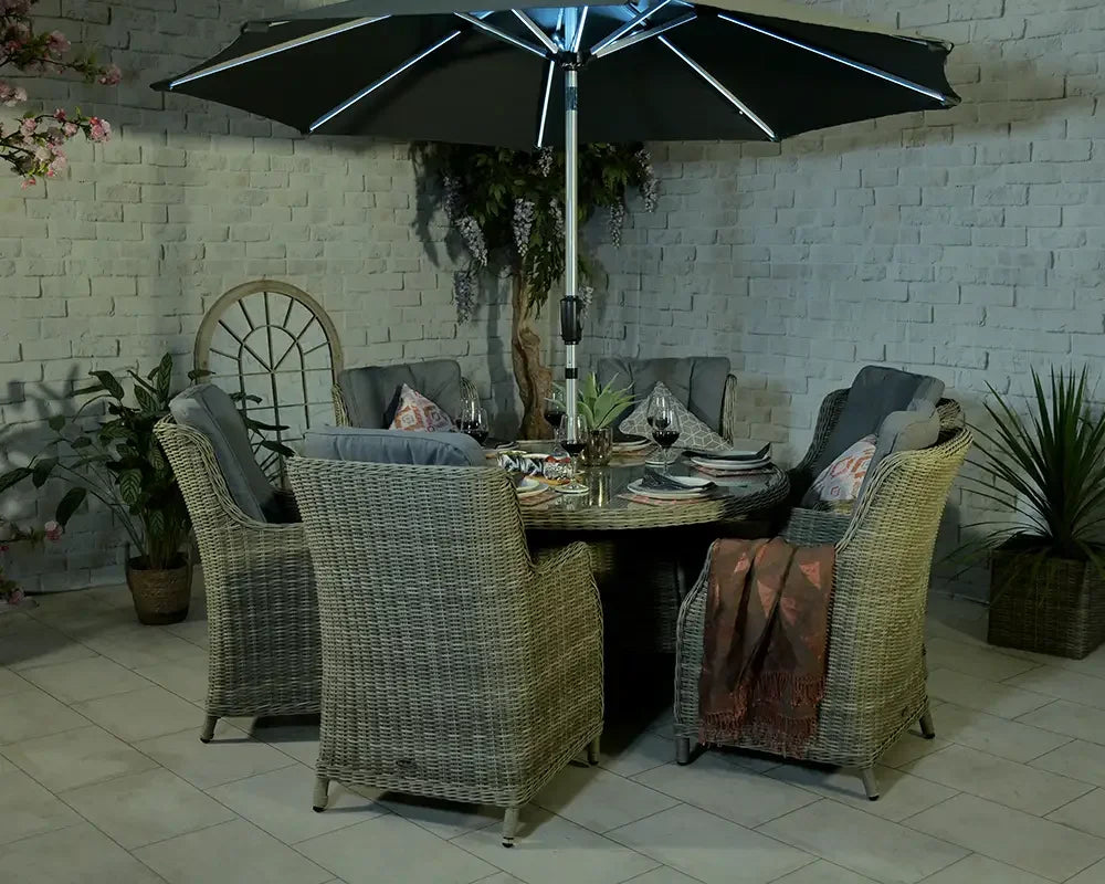 Rattan outdoor dining set with six cushioned chairs and round table under large parasol
