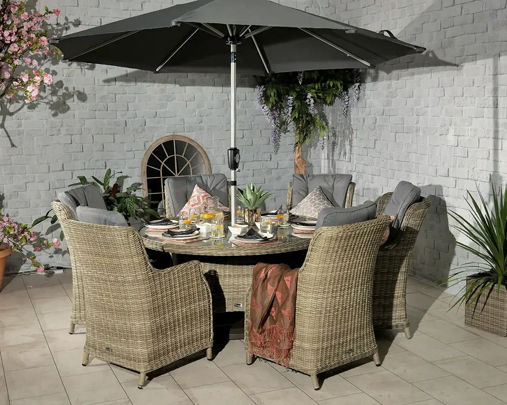 Rattan outdoor dining set with round table, six cushioned chairs and grey parasol on patio