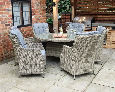 Grey rattan outdoor dining set with round glass table and six cushioned chairs on patio