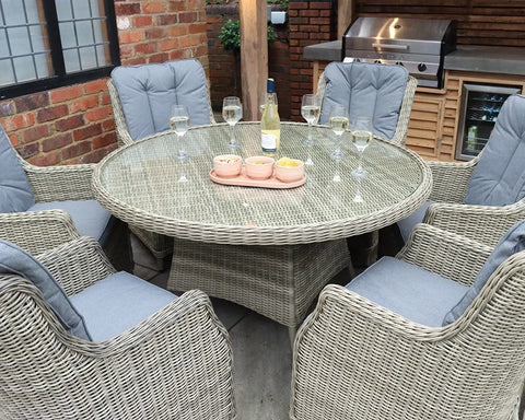 Rattan dining set with six cushioned chairs and round glass table in an outdoor patio area