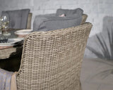 Rattan dining chair with grey cushion beside glass table set with plates and glassware