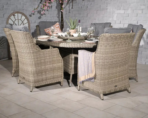 Round rattan dining set with six cushioned chairs and a table set for dinner indoors