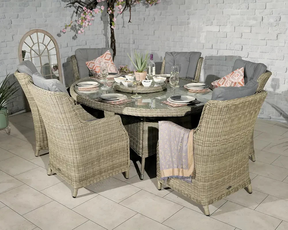 Round rattan dining set with six cushioned chairs and glass top table in indoor setting