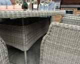 Light grey rattan dining set with glass top table and matching woven chairs outdoors