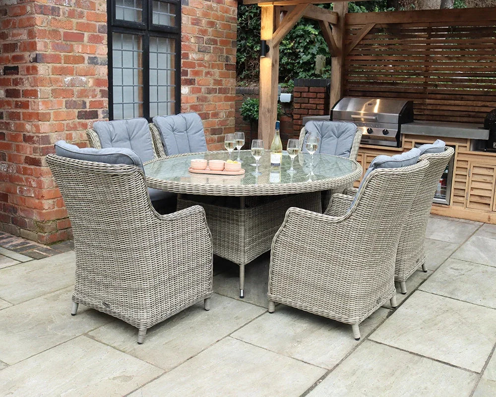Rattan outdoor dining set with six cushioned chairs and glass top table on patio