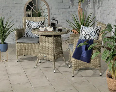 Rattan bistro set with two chairs, glass top table, grey cushions and patterned pillows
