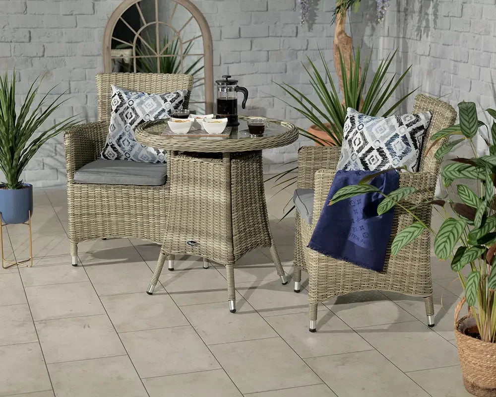 Rattan bistro set with two chairs, glass top table, grey cushions and patterned pillows