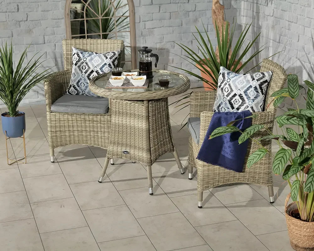 Rattan bistro set with glass-top table and two cushioned chairs in patio setting