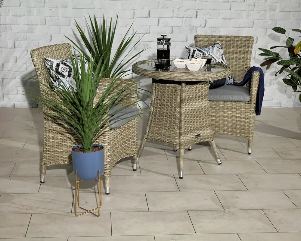 Rattan bistro set with glass top table and two cushioned chairs, indoor plant beside