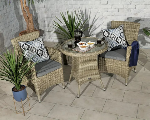 Rattan bistro set with glass-top table, two grey cushioned chairs and patterned cushions