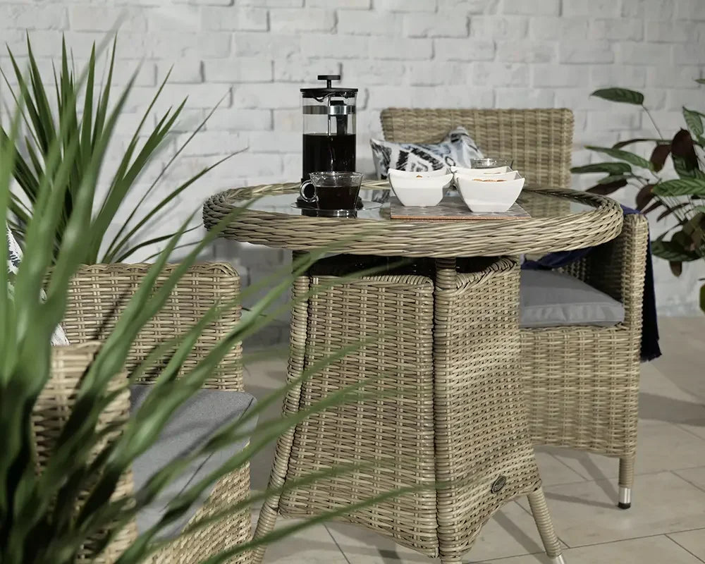 Rattan garden dining set with round glass table and two chairs on tiled floor