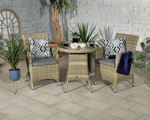 Rattan garden bistro set with glass-topped table and two cushioned chairs, indoor setting
