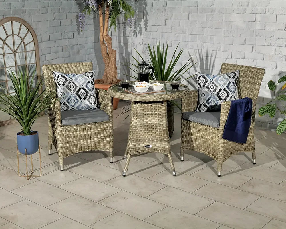 Rattan garden bistro set with glass-topped table and two cushioned chairs, indoor setting