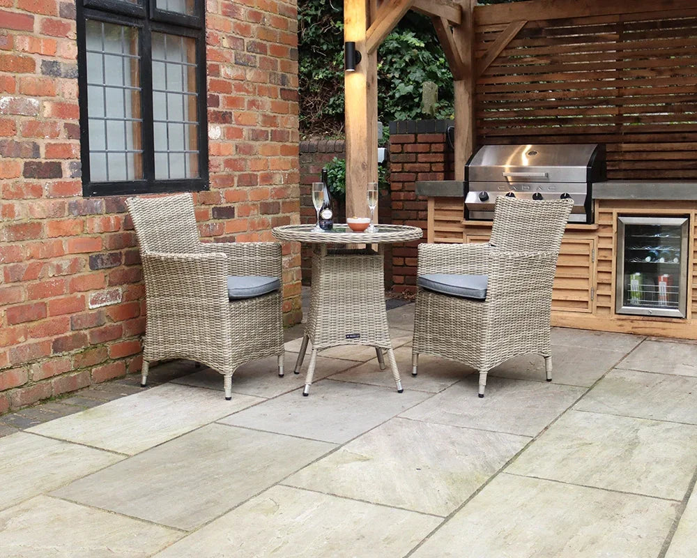 Rattan bistro set with two cushioned chairs and round table on stone patio near barbecue area