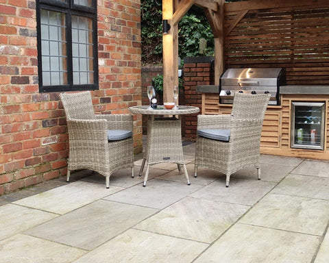 Rattan bistro set with two cushioned chairs and round table on stone patio near barbecue area