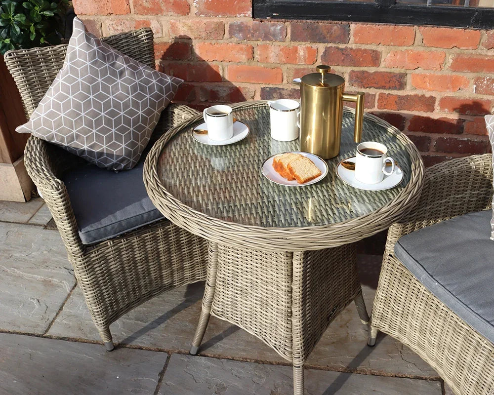 Rattan bistro garden set with glass table, two chairs, coffee cups and cake outdoors