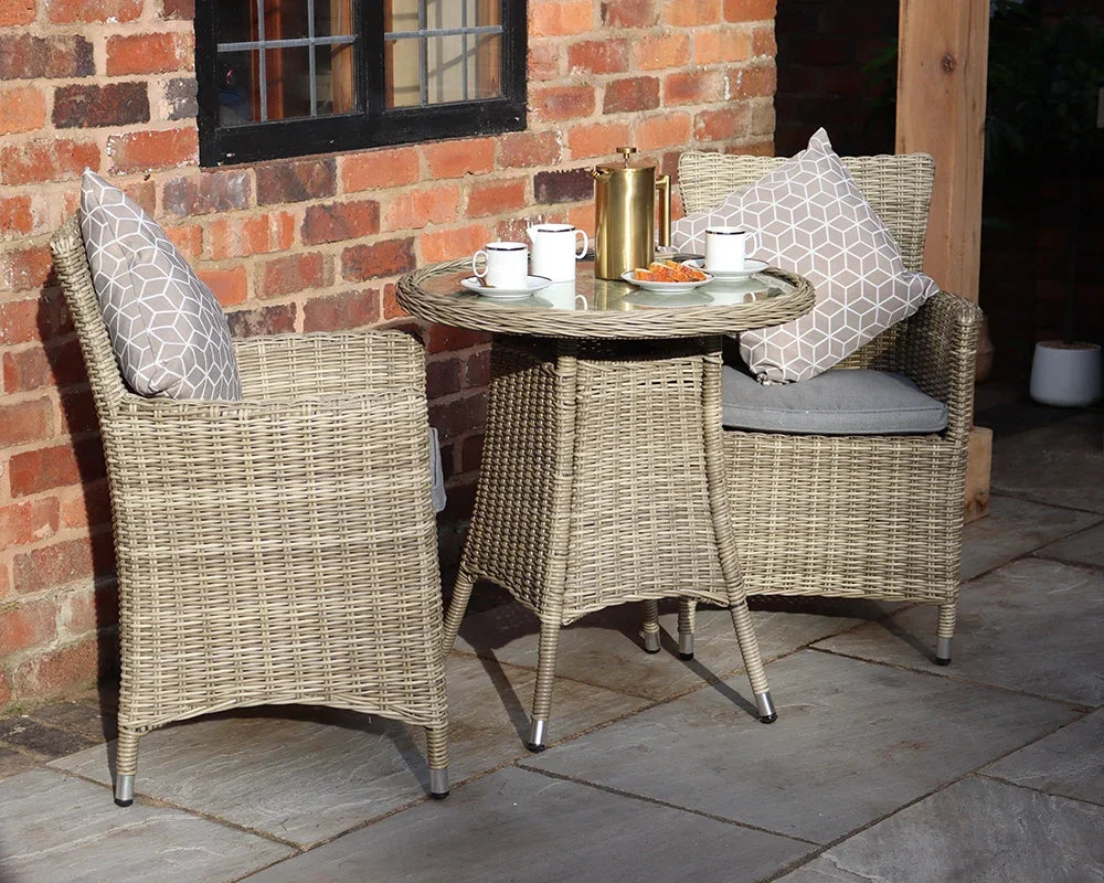 Rattan bistro set with two cushioned chairs and round table on patio, mugs and snacks on top