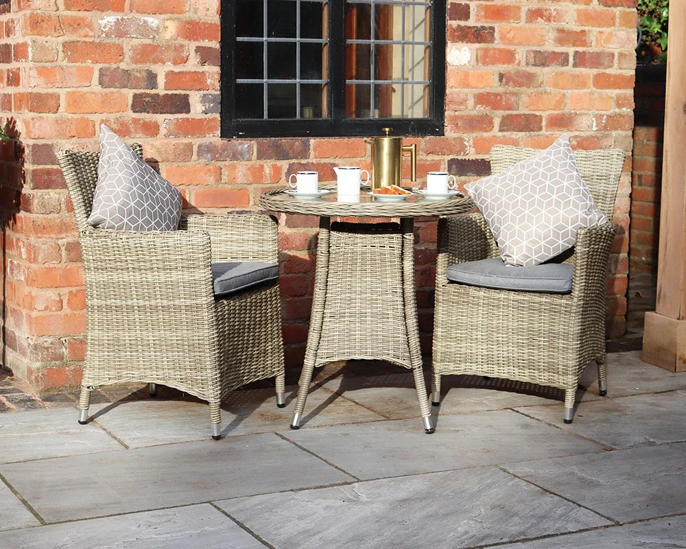 Rattan garden bistro set with round table, two armchairs, cushions and coffee cups outdoors
