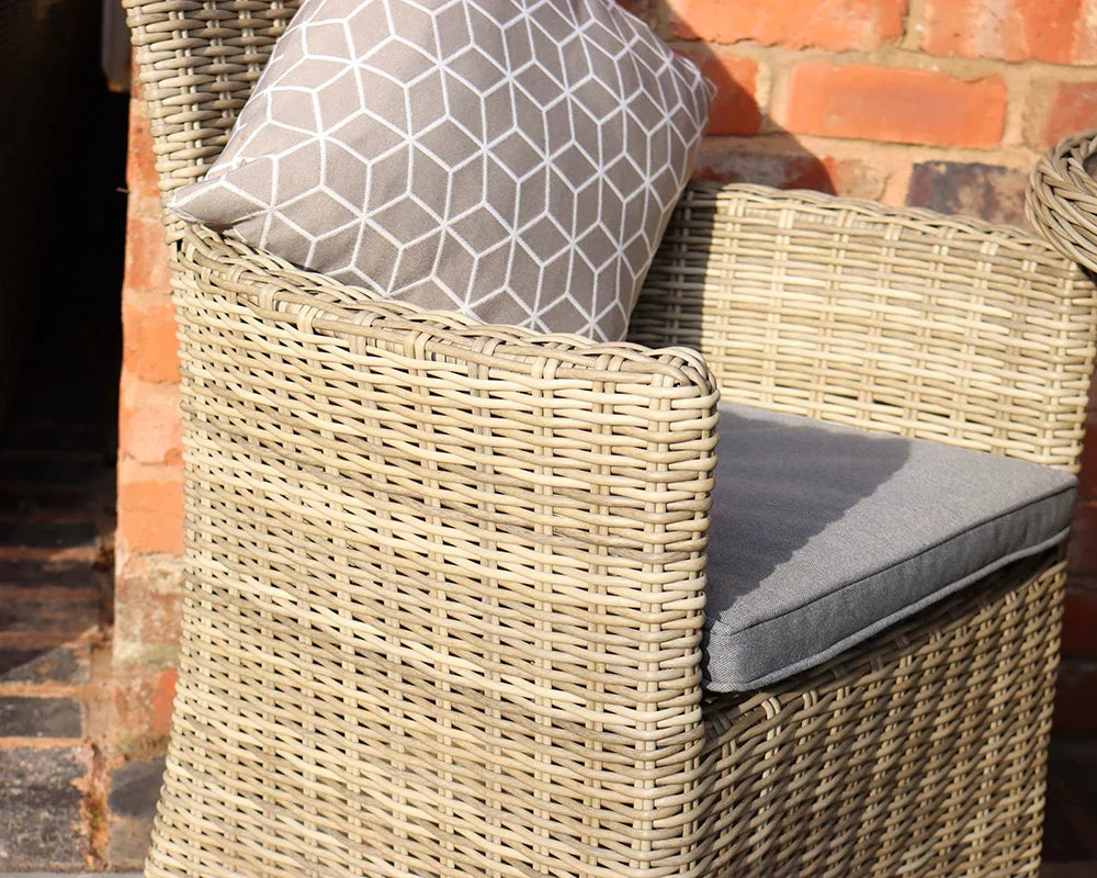 Rattan garden armchair with grey seat cushion and geometric-pattern pillow against brick wall