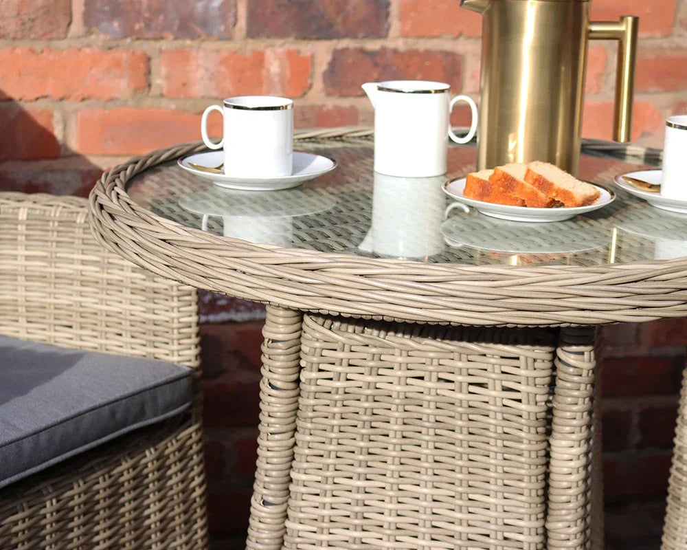 Rattan garden table set with glass top, two cups, plates, and a brass jug outdoors