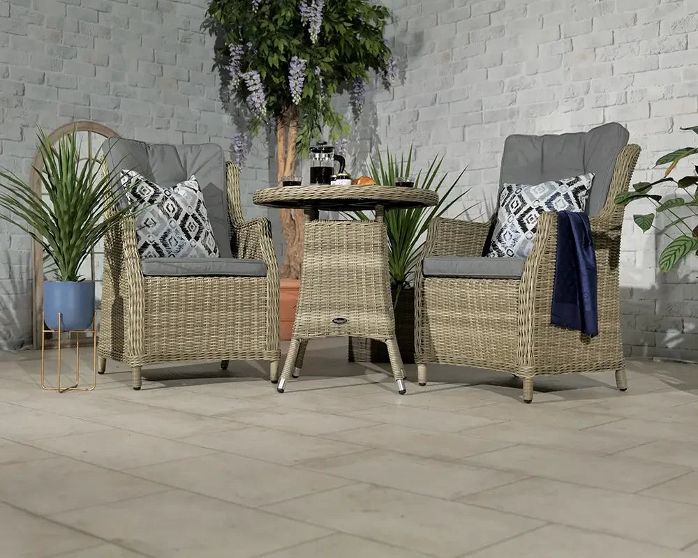 Rattan garden bistro set with glass top table, two cushioned chairs, and decorative plants