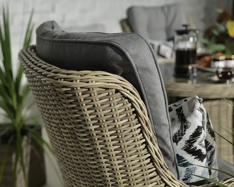 Close up of rattan garden chair with grey cushion and printed pillow, glass table in background