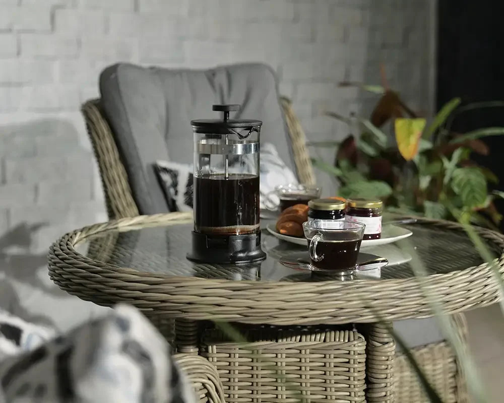 Rattan garden furniture set with glass top table, French press, coffee cup, and breakfast items
