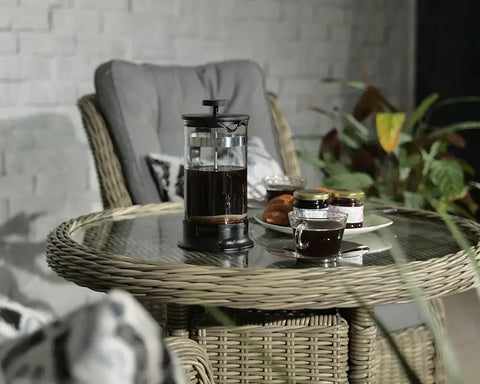 Rattan garden furniture set with glass top table, French press, coffee cup, and breakfast items